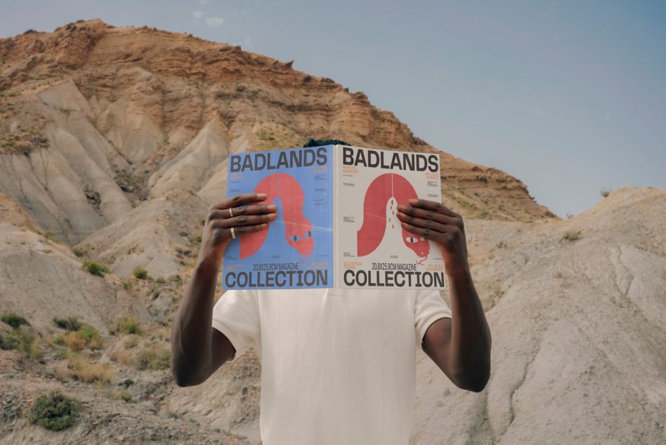 Man holding magazine mockups in front of face standing against desert landscape, design showcase, print presentation, creative outdoor shot.