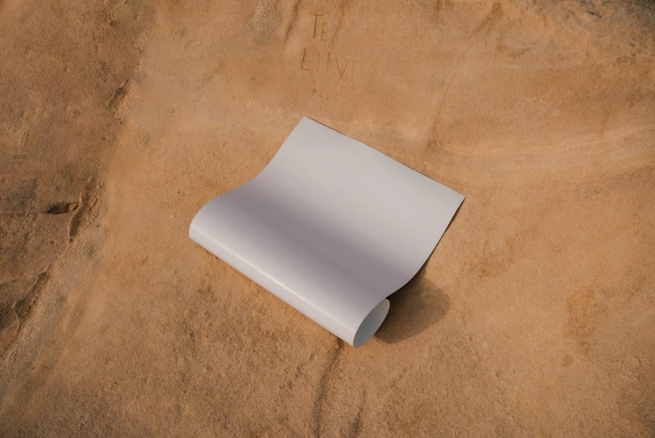 White curved paper mockup casting shadow on sand surface