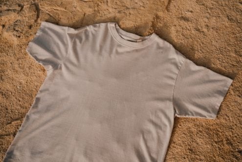Plain cream colored t-shirt on textured sandy background flat lay