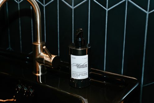 Elegant black soap dispenser on dark countertop with bronze tap, showcasing modern packaging design, ideal for mockups and product templates.