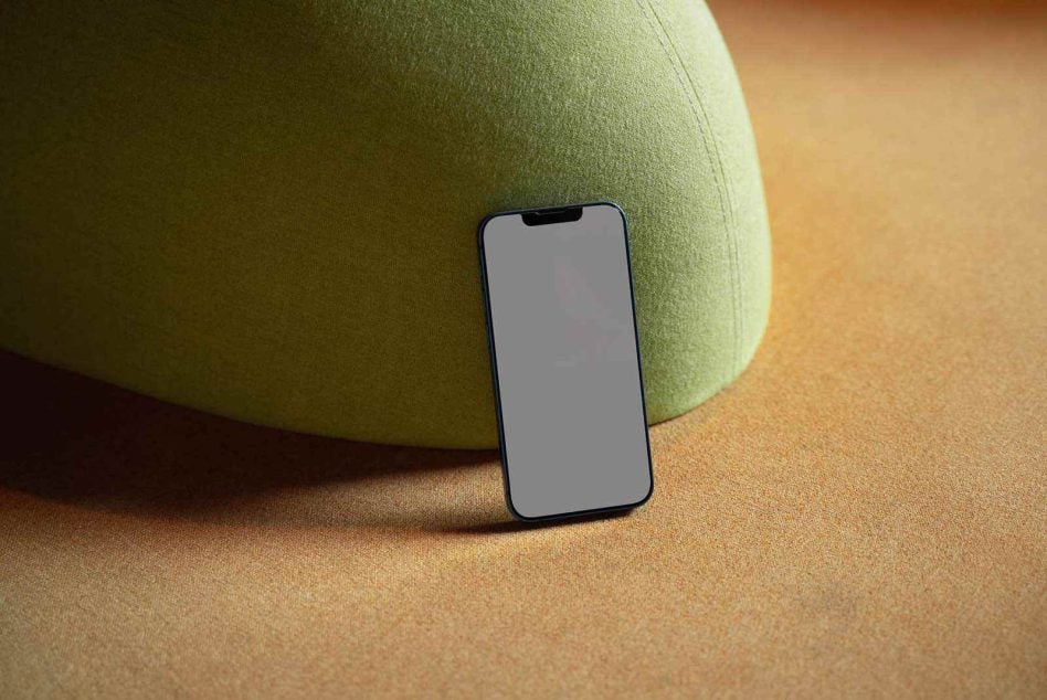 Dark blue phone leaning against sage green fabric sphere on neutral background