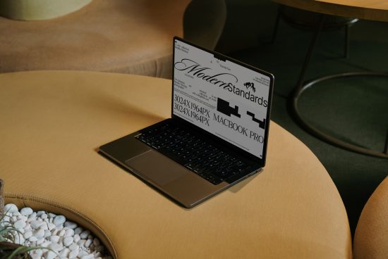 Laptop on a mustard sofa displaying a font design mockup, perfect for presentations in modern workspace settings, suitable for design professionals.