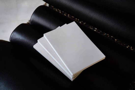 Stack of blank white paper on dark leather couch for mockup design presentation, elegant stationery layout, paper quality display.