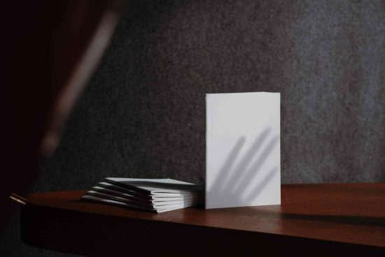 Mockup of blank white vertical business cards stacked on a wooden desk with atmospheric shadows, perfect for brand presentation.