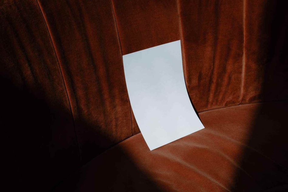 Single blank page mockup resting on deep terracotta velvet upholstery