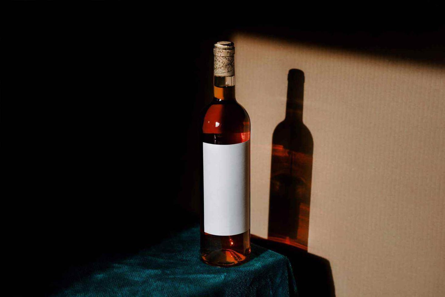 Wine bottle with blank label mockup on dark fabric, dramatic lighting for product design, ideal for graphics and branding presentations.