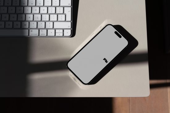 Smartphone mockup on desk next to keyboard with natural shadows, ideal for UI/UX design presentations, digital assets for designers.