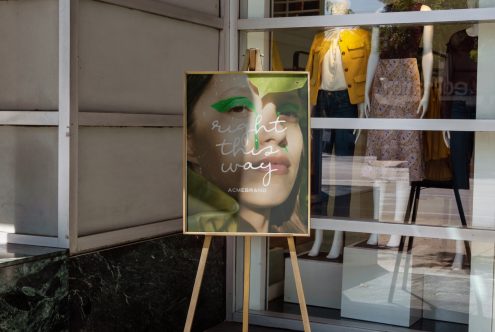 Elegant outdoor poster mockup on easel displaying beauty ad with text "right this way", against a boutique store backdrop for designers.