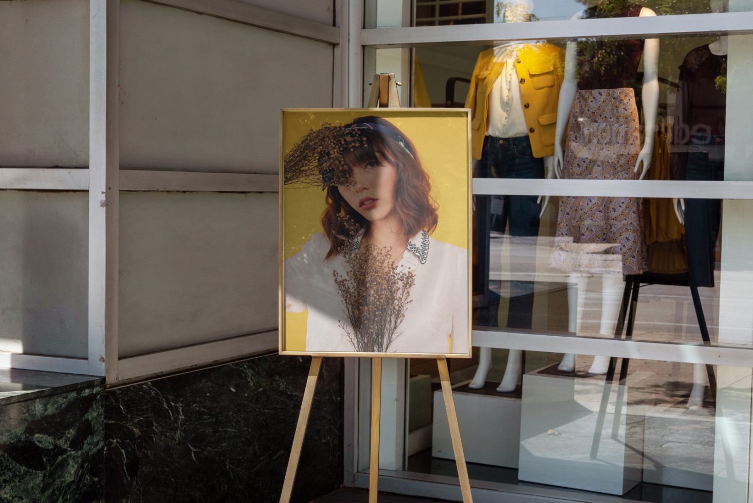 Elegant poster mockup display outside boutique, stylish woman portrait, trendy fashion shop storefront, urban design.