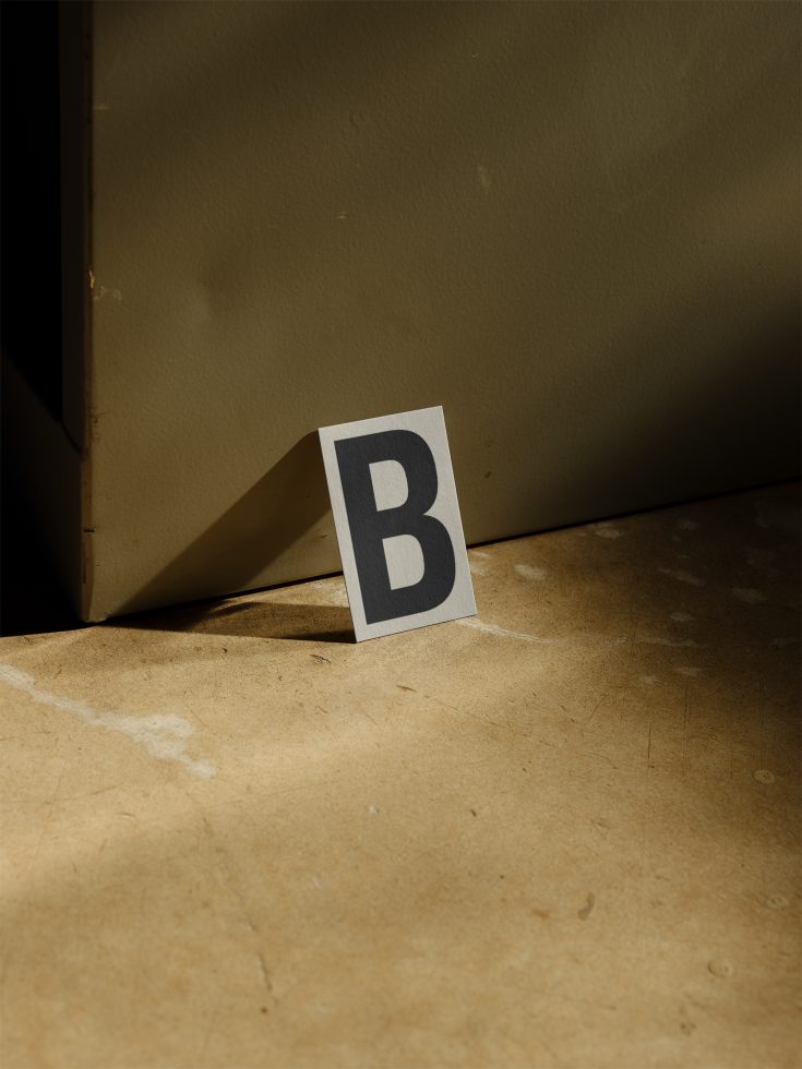 Minimalistic font design 'B' card standing against a backdrop with dramatic shadows for graphic design mockup.