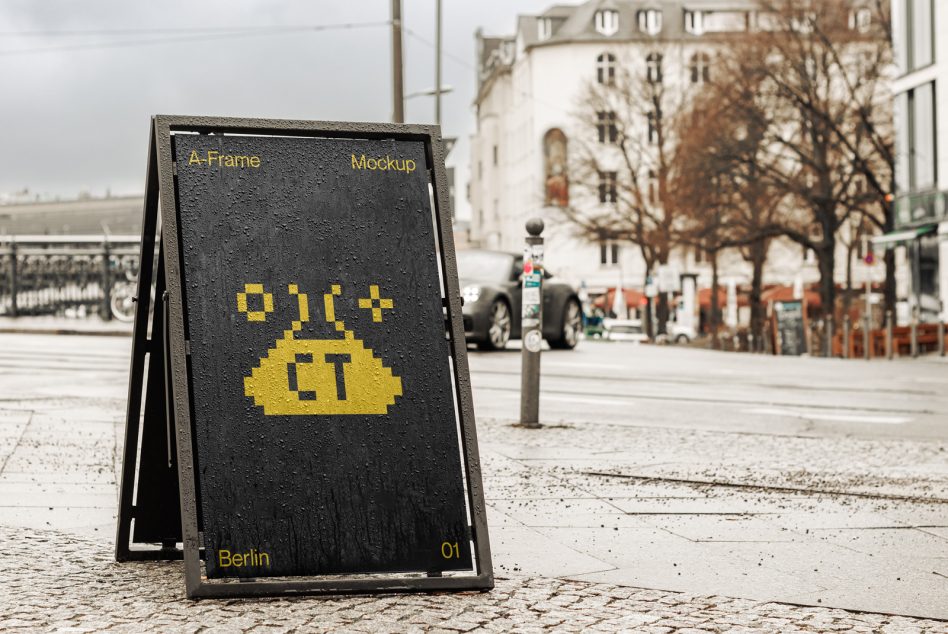 Black A-frame sandwich board with yellow pixel graphic on city plaza
