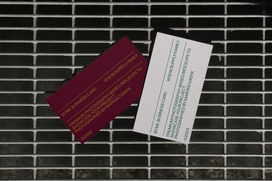 Burgundy business card tilted left next to white card on brick wall backdrop
