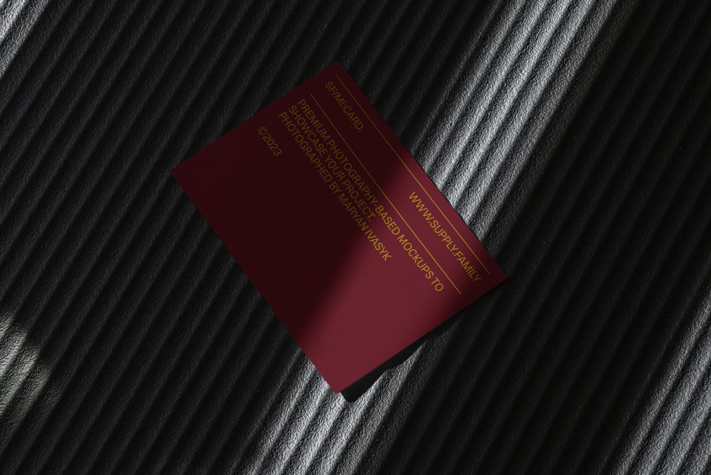 Elegant business card mockup with a maroon design lying on a textured dark striped surface, ideal for designers looking to showcase branding identity.