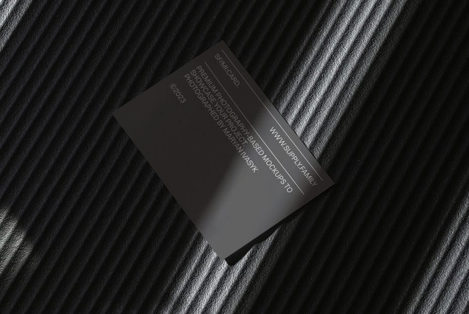 Dark business card tilted on striped fabric surface with debossed lettering