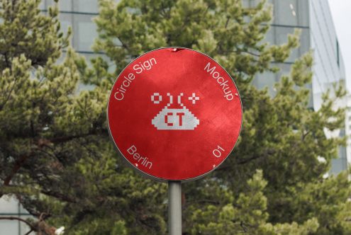 Red circular sign with white pixel alien figure, mounted on pole near trees