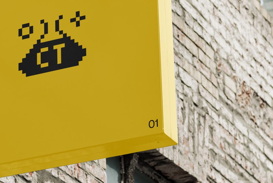 Yellow corner sign detail with black pixel art lettering on brick