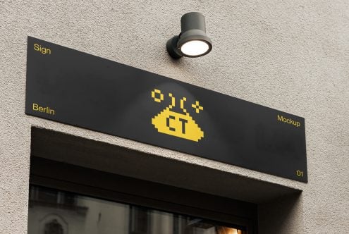 Black angled sign with yellow pixel logo on concrete wall by light