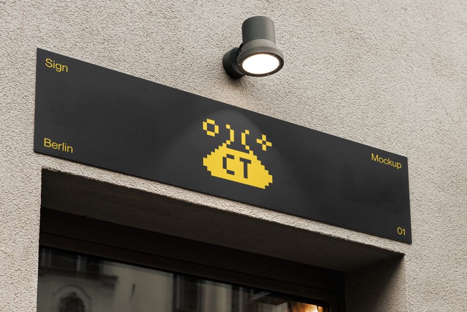 Black angled sign with yellow pixel logo on concrete wall by light