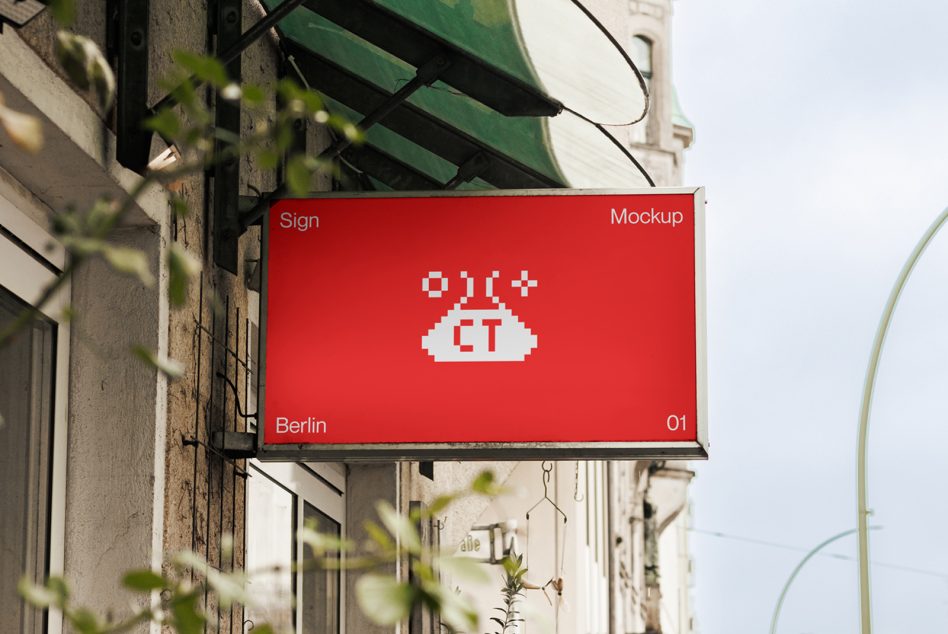 Red storefront sign with pixel art UFO logo, hanging above street plants