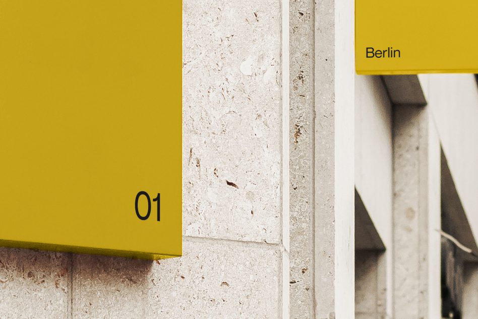 Yellow metal panel with dark numerals mounted on concrete corner edge