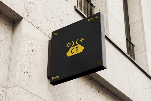 Black wall-mounted sign with yellow pixelated logo on concrete building facade