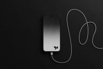 iPhone with light gradient screen next to white charging cable on dark background