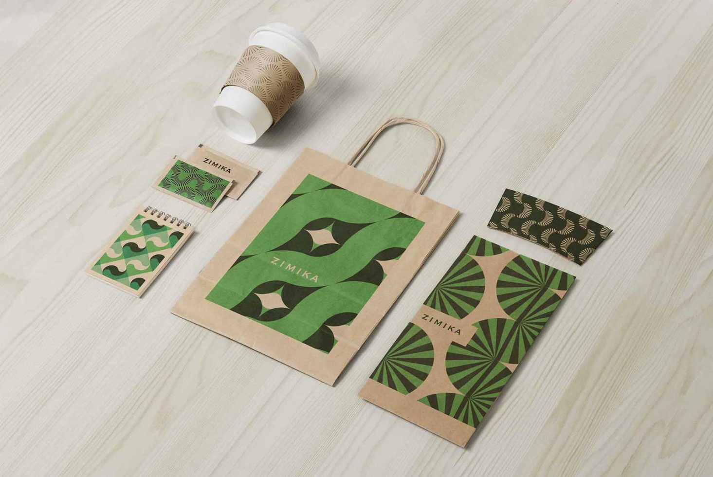 Eco-friendly branded packaging mockup set on wooden background, includes paper bag, cup, business cards, and notebook with green patterns for design.