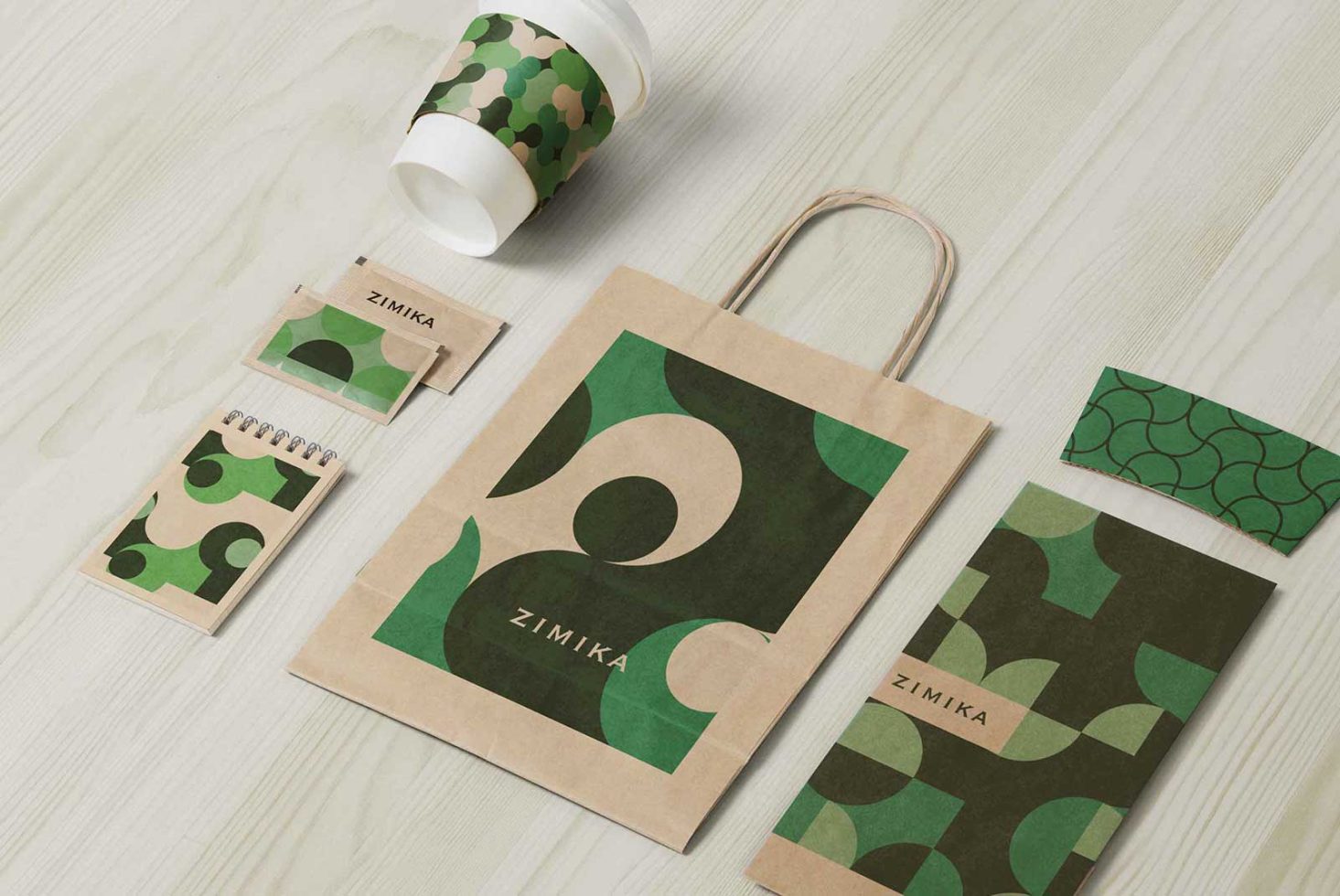 Eco-friendly packaging mockup with green camouflage patterns featuring paper bags, coffee cup, and notepads on a wooden surface.