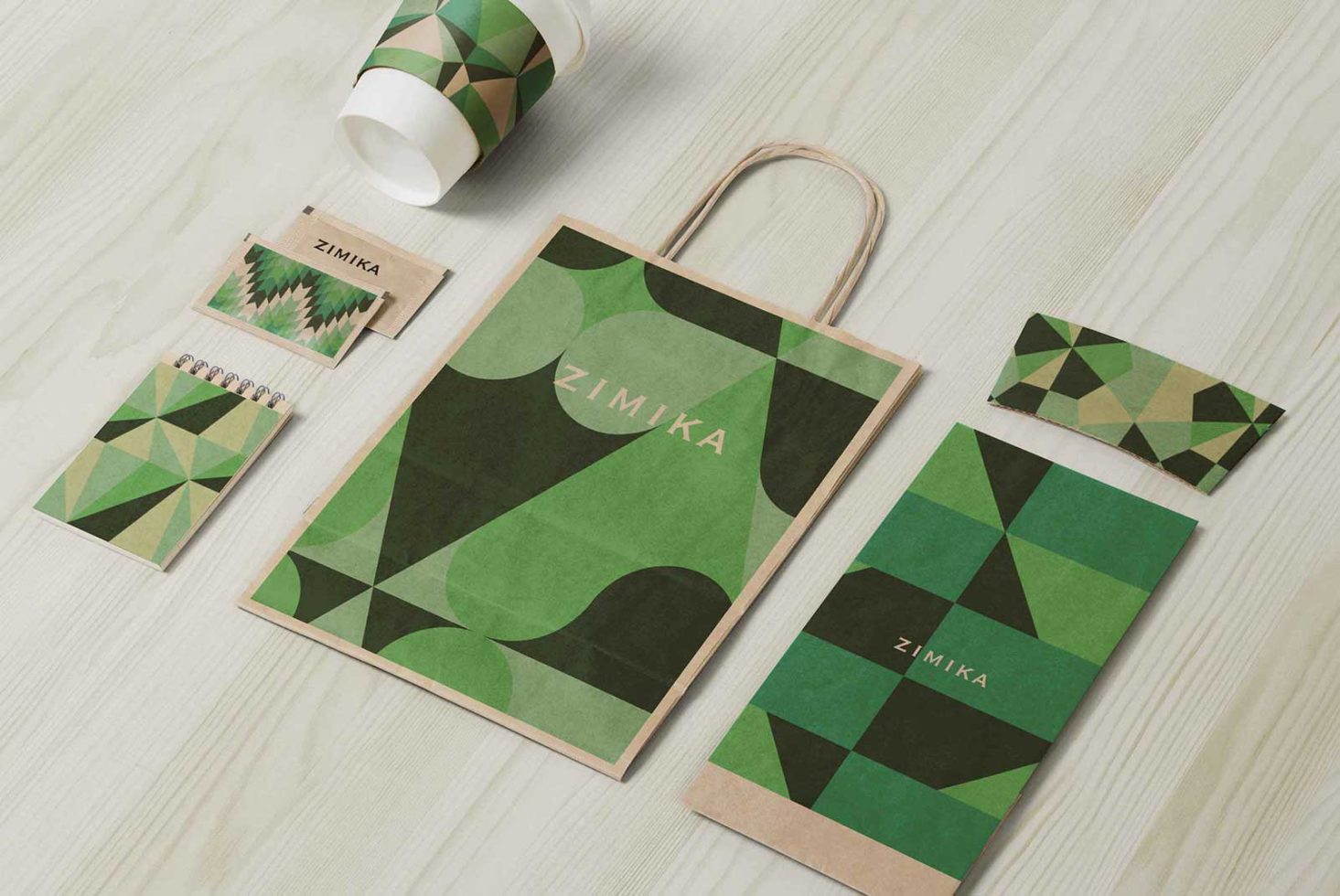 Geometric branded stationery mockup with paper bag, cup, and notepads on a wooden surface, ideal for presentations and portfolios.