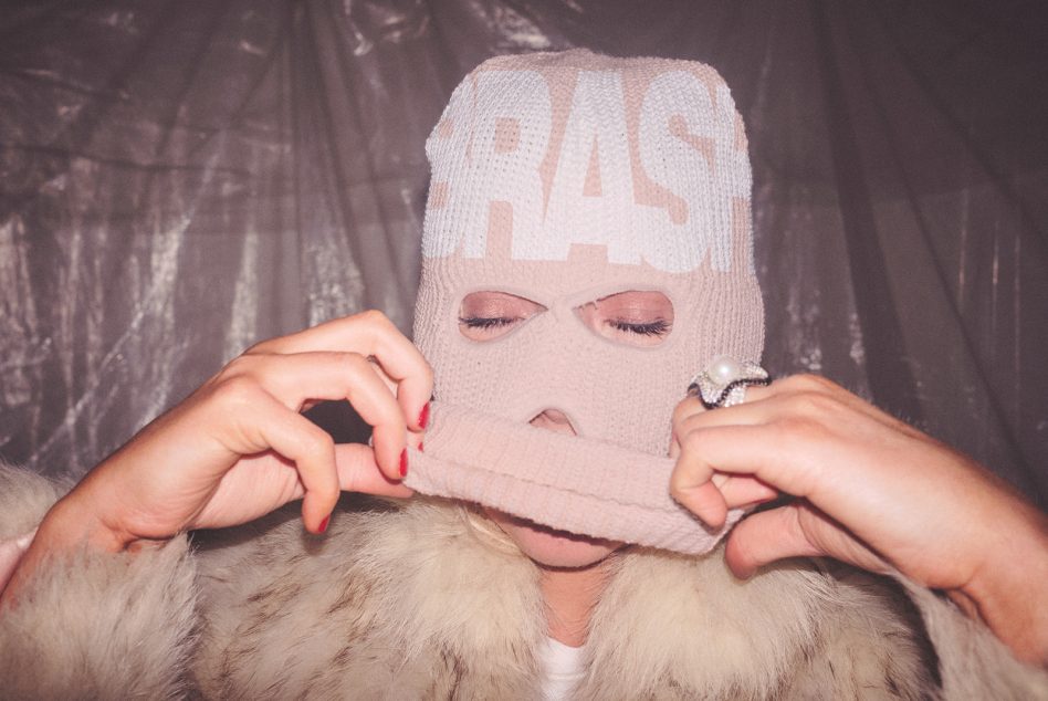 Person in cream knit balaclava with red nail polish adjusting the fabric around their face