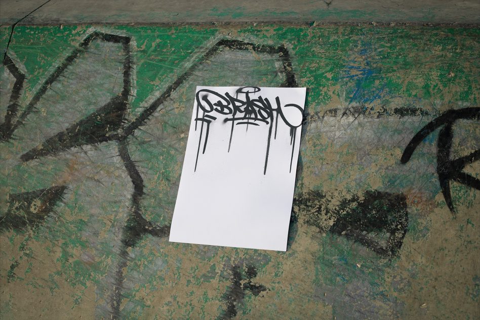 White paper with graffiti style black outline letters on weathered green brick surface