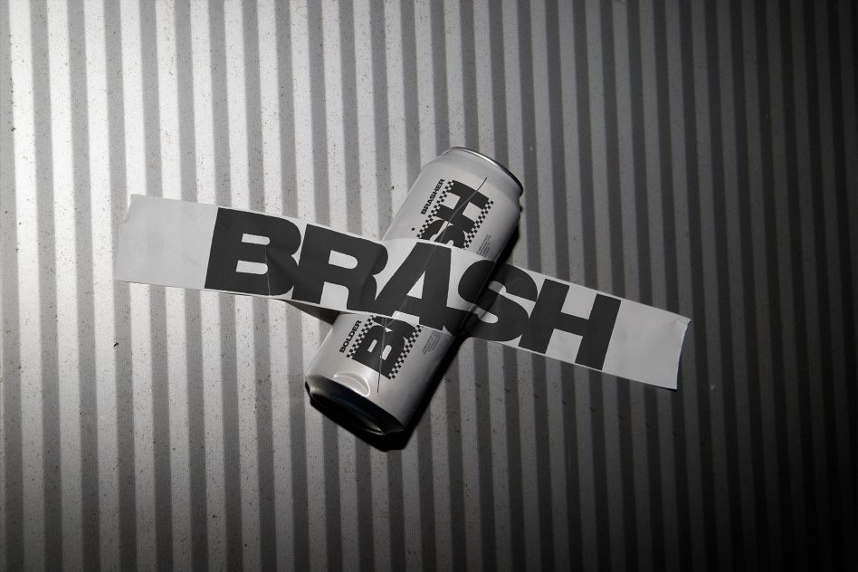 Silver soda can with BRASH text across white tape on concrete backdrop