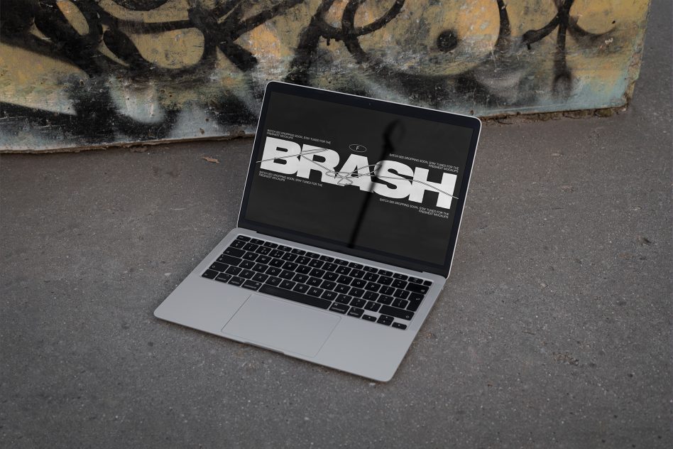 MacBook near street art showing BRASH text on dark screen mockup