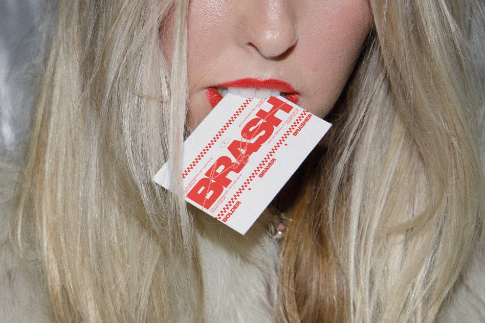 Woman with red lipstick holding white card with bold red text in mouth