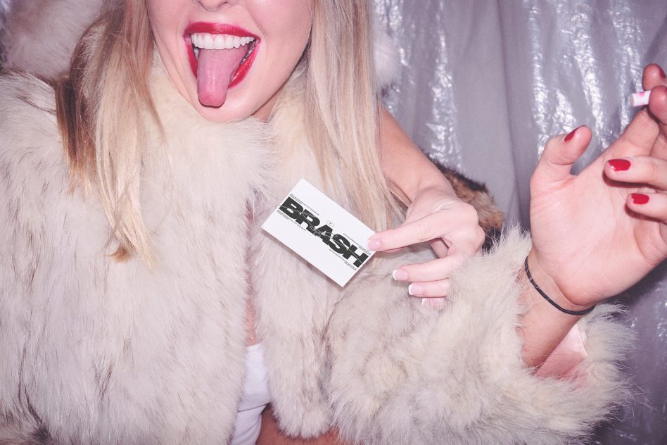 Girl in fuzzy coat holding white business card mockup against sequin backdrop