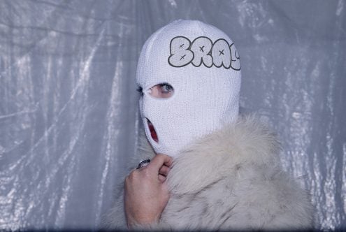 White knit ski mask with graffiti-style text on forehead, worn with white fur collar