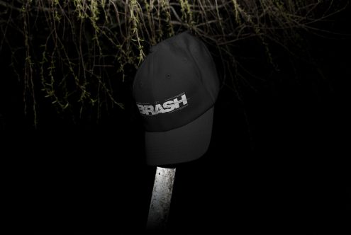 Black dad hat with metallic BRASH logo on front against dark background
