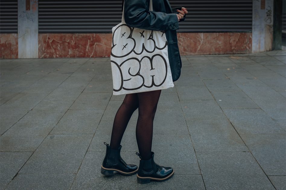 White canvas tote bag with black cloud outline doodles held by person in boots