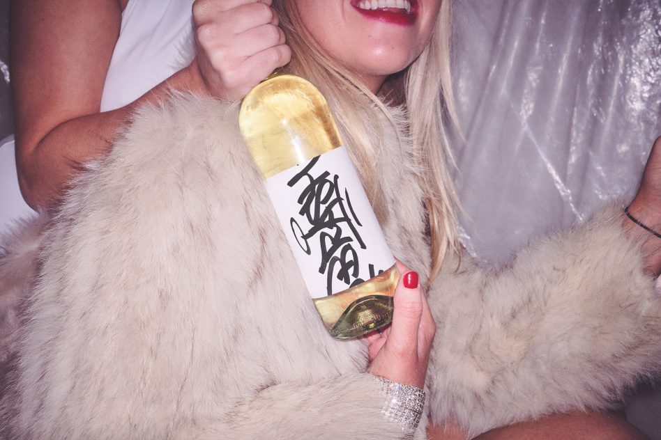 Gold wine bottle with white label held against white fur coat by woman