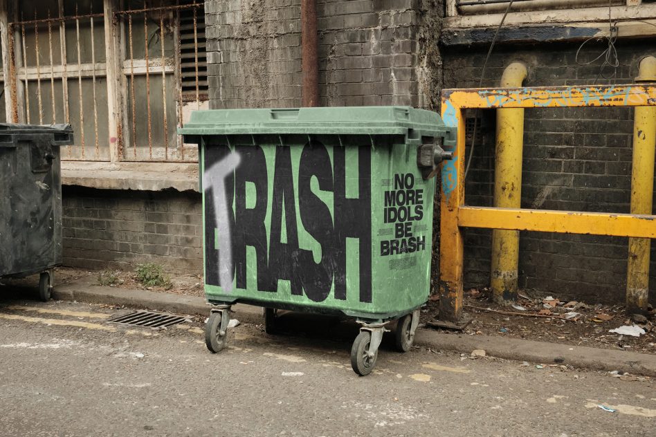 Green dumpster trash bin mockup with black graffiti text no more idols be brash