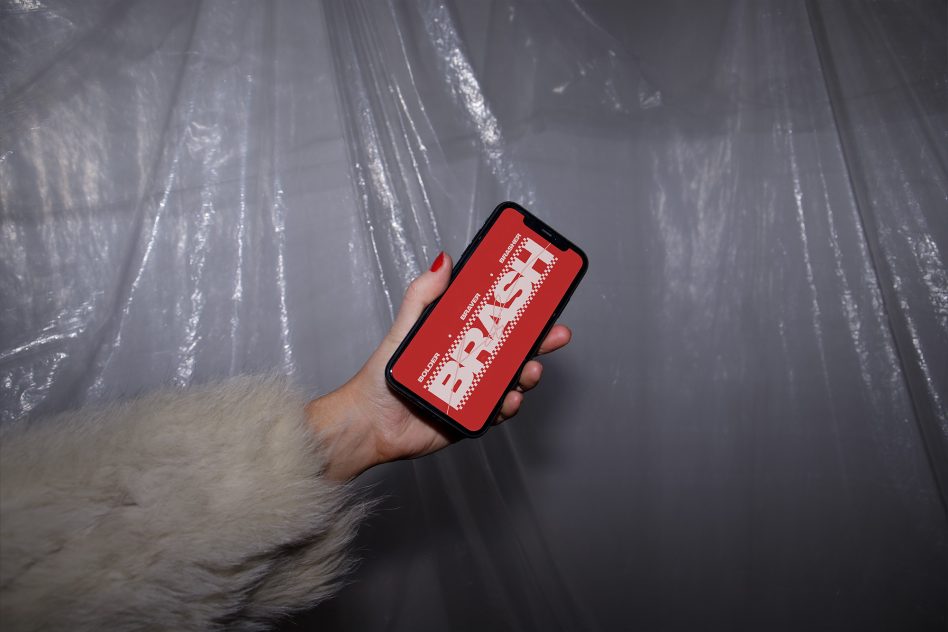 Hand holding phone with red screen displaying pixelated brand logo on shiny fabric backdrop