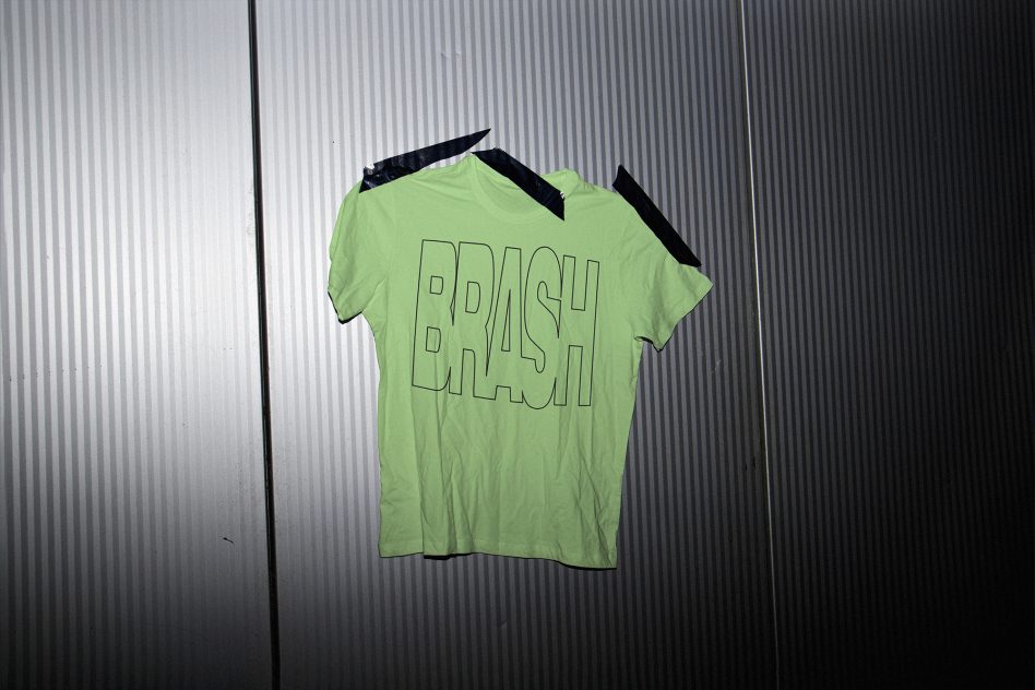 Neon green shirt outlined brash text on corrugated metal backdrop