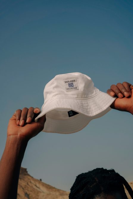 Person holding a white bucket hat with Badlands collection embroidery against a blue sky, ideal for fashion mockups and apparel design.