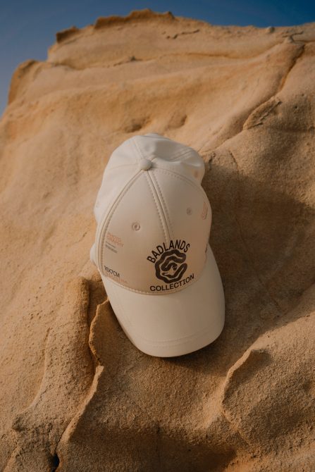 Beige baseball cap with logo mockup on sandy rock, natural outdoor lighting, product design presentation, clothing accessory, stylish headwear.