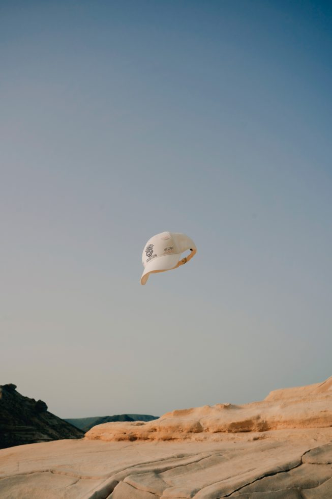 Cap mockup floating above desert landscape, clear blue sky background, outdoor hat design display, apparel graphics showcase.