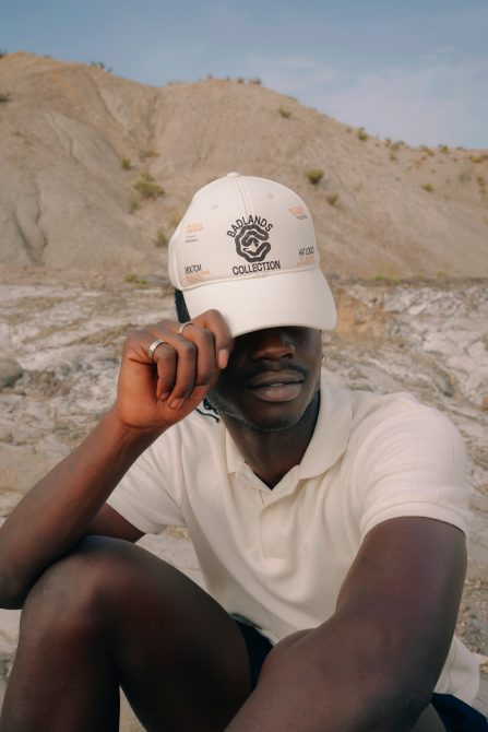 Young male model in white polo and cap posing for lifestyle mockup with earthy backdrop, ideal for branding designs.