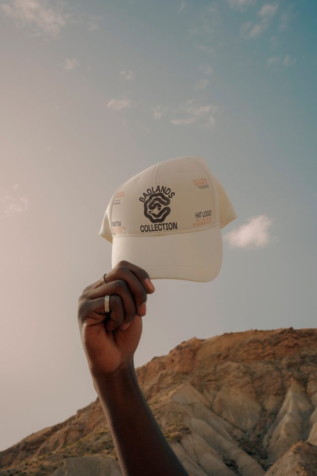 Hand holding white cap with logo mockup against a clear sky and rocky background, ideal for designers looking for apparel presentation.