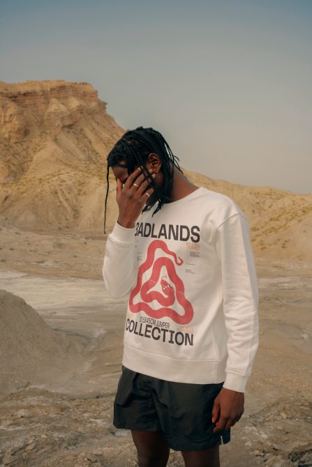 Man in white graphic sweatshirt and black shorts posing in a desert for fashion mockup template. Ideal for apparel design presentations.