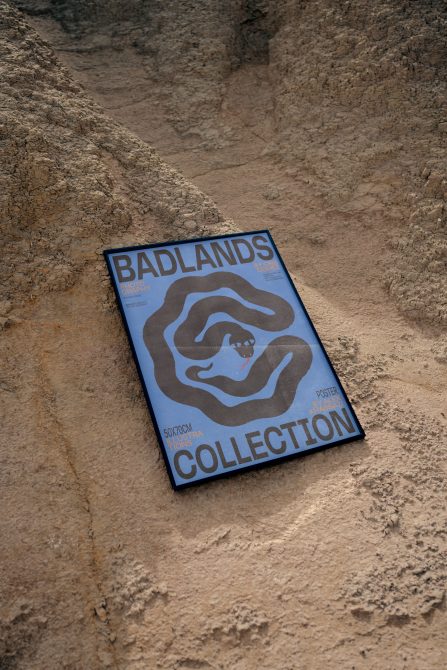 Blue Badlands Collection poster laying on sandy desert ground