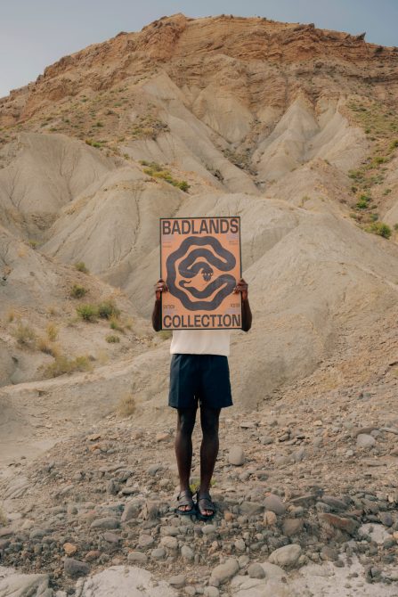 Person holding a retro style poster with 'Badlands Collection' text in a desert environment, perfect for outdoor graphics or poster mockups.